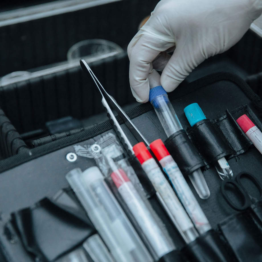 Gloved hand handling test tube in forensic equipment case at crime scene.