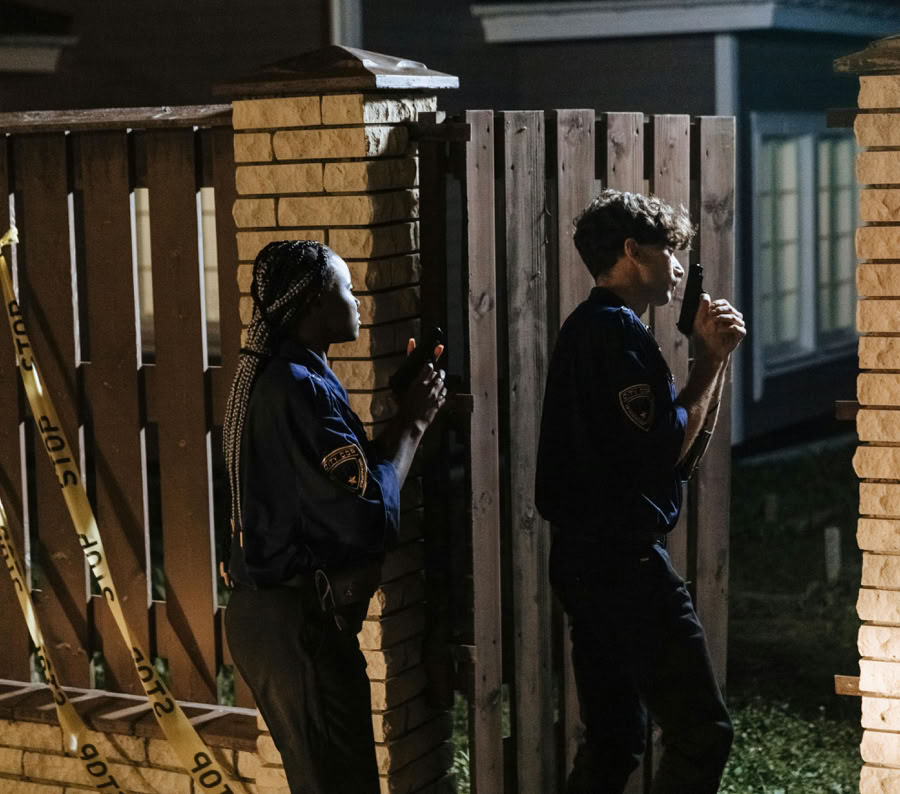 Two police officers investigate a crime scene at night, entering a house with caution.