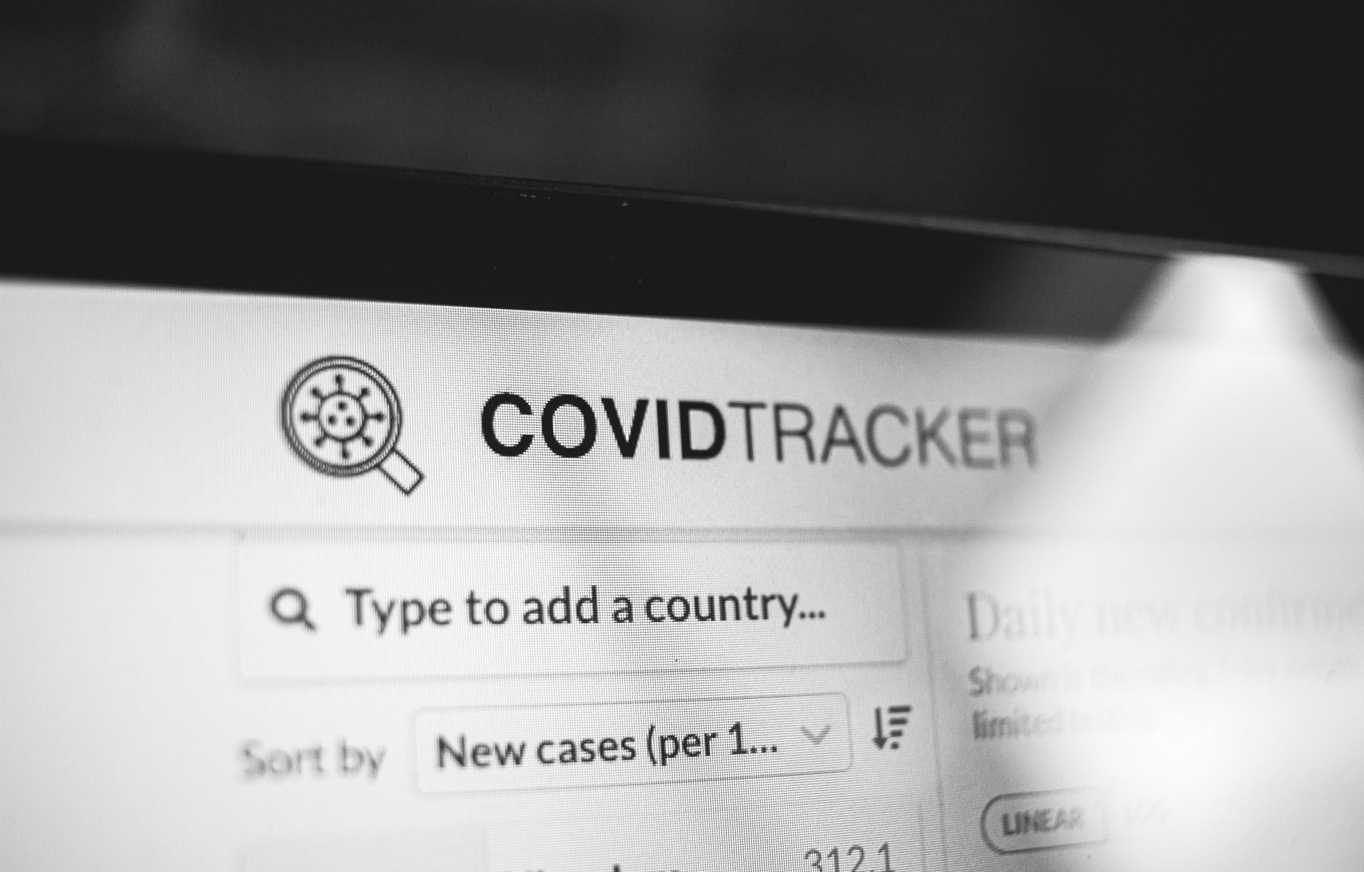 Black and white image showing COVID-19 tracker on a laptop screen with search options.