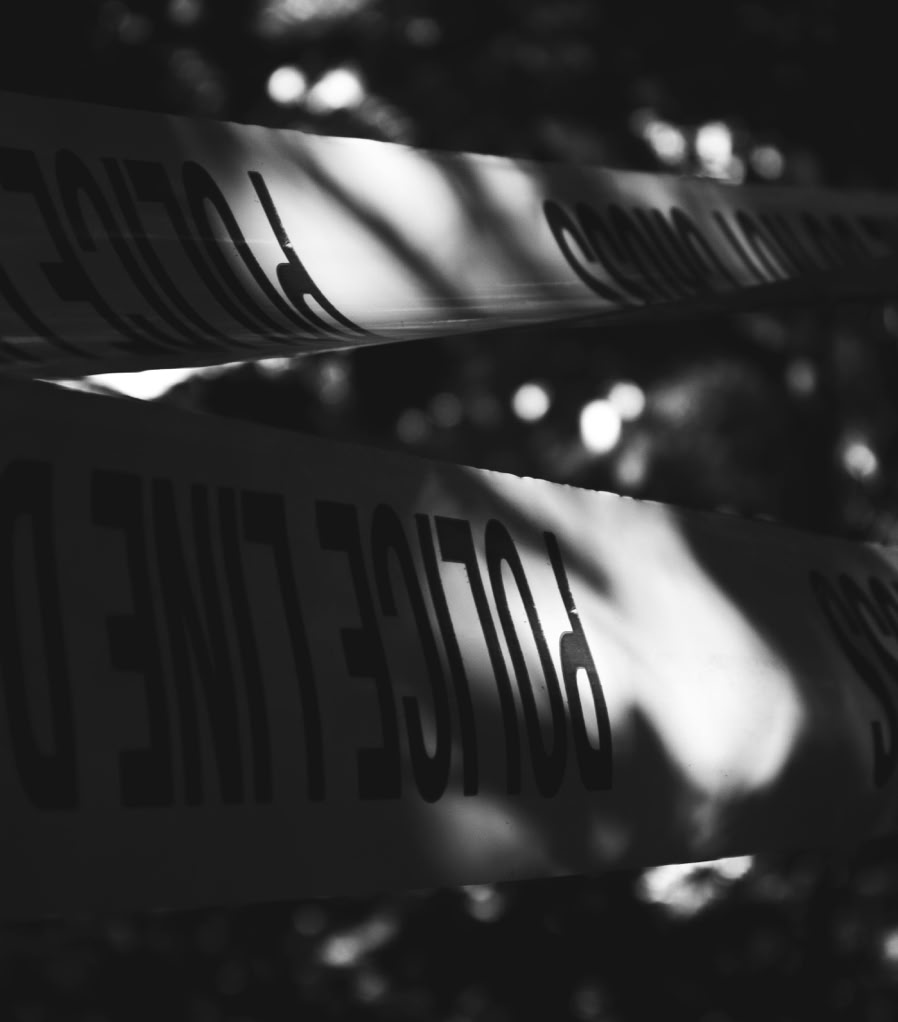 Black and white image of police tape in an outdoor setting, casting dramatic shadows.